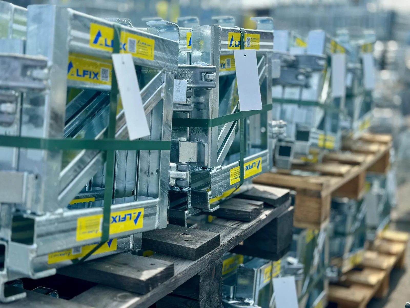 Metalliset rakennustelineet on pakattu lavoille, sidottu vihreällä nauhalla ja niissä on valkoiset etiketit. Kirkas valaistus korostaa metallin kiiltoa.